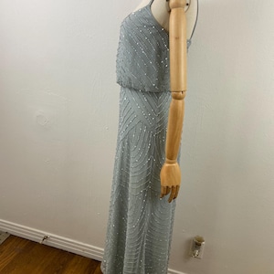 K&ouml;nnte beinhalten: Ein hellblaues Abendkleid mit Perlenbesatz. Das Kleid hat ein eng anliegendes Oberteil mit Spaghettitr&auml;gern und einen flie&szlig;enden Rock. Die Perlen erzeugen einen schimmernden Effekt und verleihen dem Kleid Eleganz.