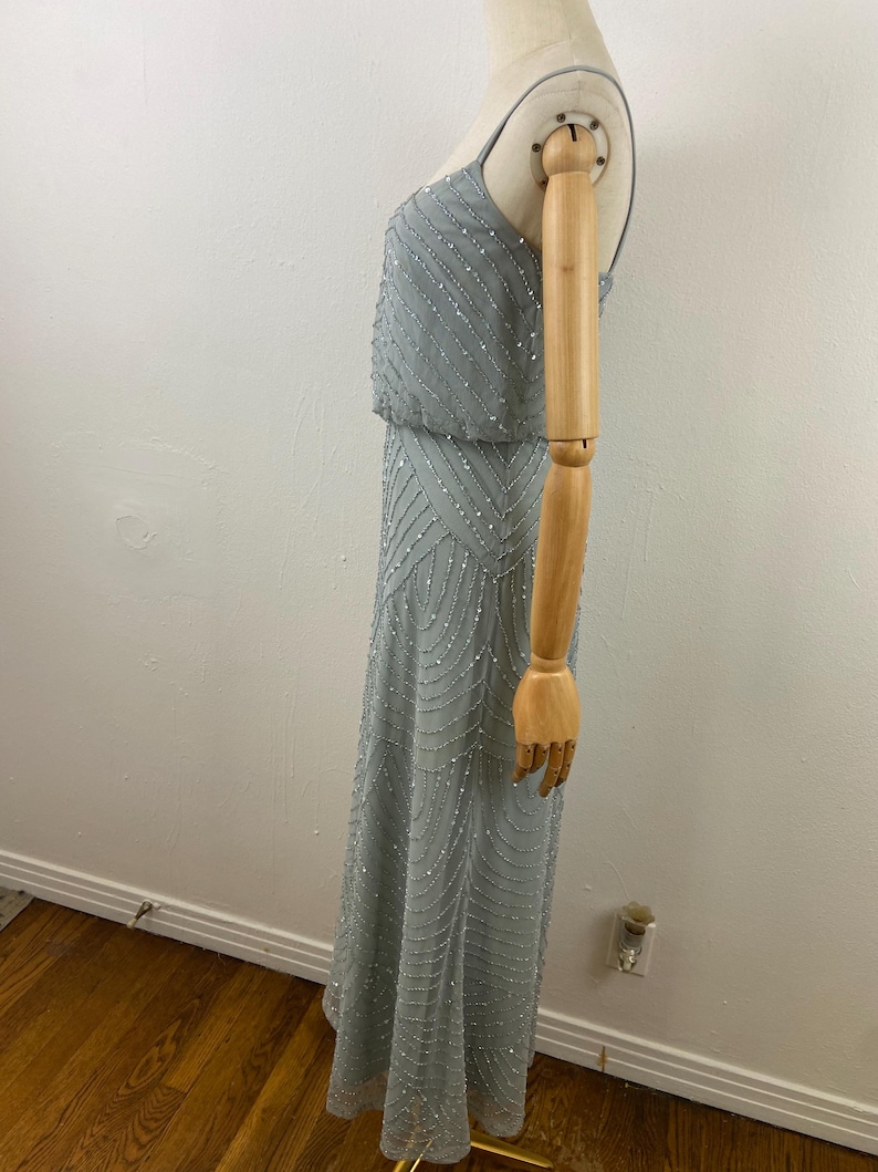 K&ouml;nnte beinhalten: Ein hellblaues Abendkleid mit Perlenbesatz. Das Kleid hat ein eng anliegendes Oberteil mit Spaghettitr&auml;gern und einen flie&szlig;enden Rock. Die Perlen erzeugen einen schimmernden Effekt und verleihen dem Kleid Eleganz.