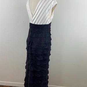 May include: A formal black evening gown with a white, striped bodice and a tiered, ruffled skirt. The dress has a V-neckline and cap sleeves. The skirt is floor-length.