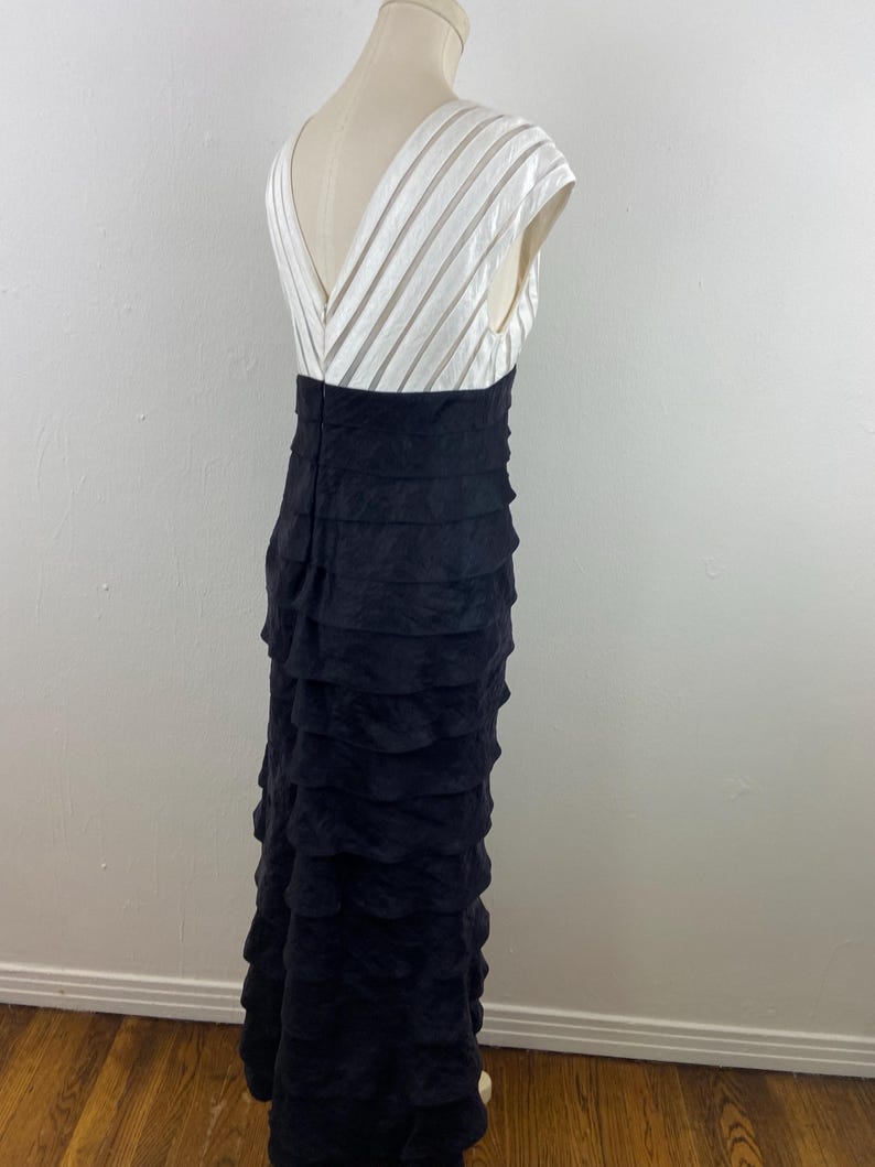 May include: A formal black evening gown with a white, striped bodice and a tiered, ruffled skirt. The dress has a V-neckline and cap sleeves. The skirt is floor-length.