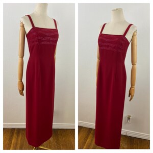 Op de afbeelding: Een lange, rode avondjurk met een vierkante halslijn en dunne bandjes. De bodice heeft een gestructureerd, golfachtig ontwerp. De jurk wordt op een mannequin getoond en toont zijn vloerlange silhouet. De jurk heeft een effen, dieprode kleur.