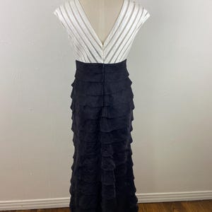 May include: A formal gown with a white, striped bodice and a black, tiered skirt. The dress has a V-neckline and a fitted waist. The skirt is floor-length and made of a textured fabric.