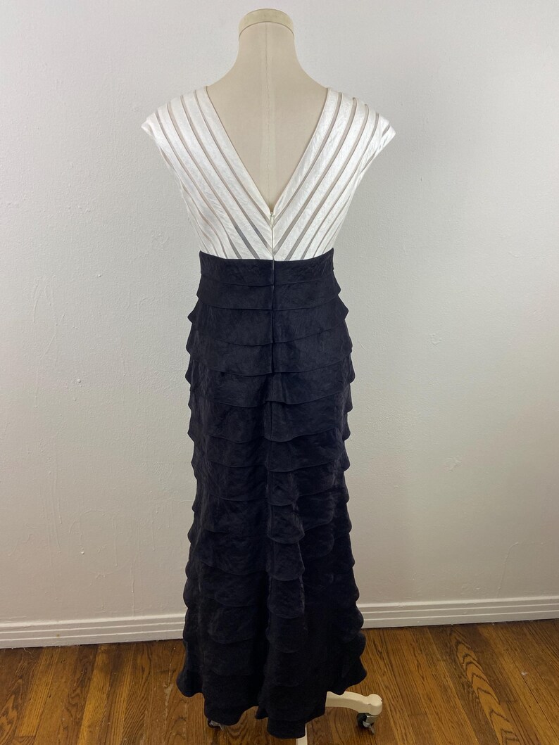 May include: A formal gown with a white, striped bodice and a black, tiered skirt. The dress has a V-neckline and a fitted waist. The skirt is floor-length and made of a textured fabric.
