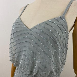 K&ouml;nnte beinhalten: Hellblaues Kleid mit V-Ausschnitt und Spaghettitr&auml;gern. Das Kleid ist mit Reihen silberner Pailletten in einem Zickzackmuster verziert. Das Oberteil hat ein mehrschichtiges Design, das dem eleganten Abendkleid Tiefe verleiht.