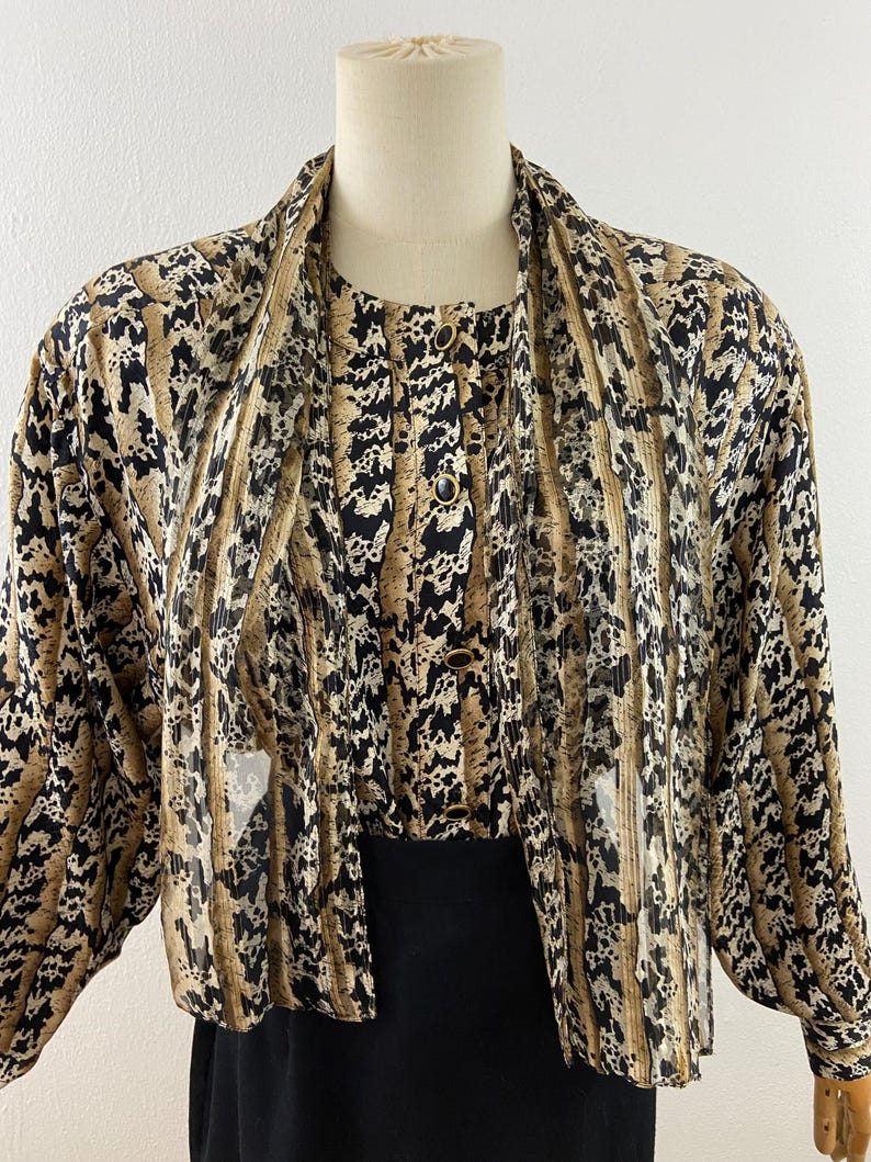 Peut inclure: Ensemble vintage deux pi&egrave;ces avec un haut &agrave; motifs et un bas noir uni. Le haut pr&eacute;sente un design boutonn&eacute; avec un motif unique dans les tons marron, noir et beige. L'ensemble est pr&eacute;sent&eacute; sur un mannequin, mettant en valeur son style.