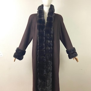 May include: A long brown coat with a fur collar and cuffs. The fur is a dark brown colour and is arranged in a horizontal pattern. The coat is lined with a brown fabric.