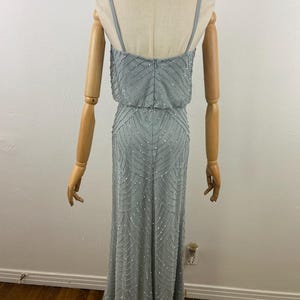 K&ouml;nnte beinhalten: Ein hellblaues Abendkleid mit Perlenbesatz. Das Kleid hat d&uuml;nne Spaghettitr&auml;ger und ein eng anliegendes Oberteil, das in einen bodenlangen Rock &uuml;bergeht. Die R&uuml;ckseite des Kleides ist sichtbar und zeigt den Rei&szlig;verschluss und die aufwendigen Perlenarbeiten.