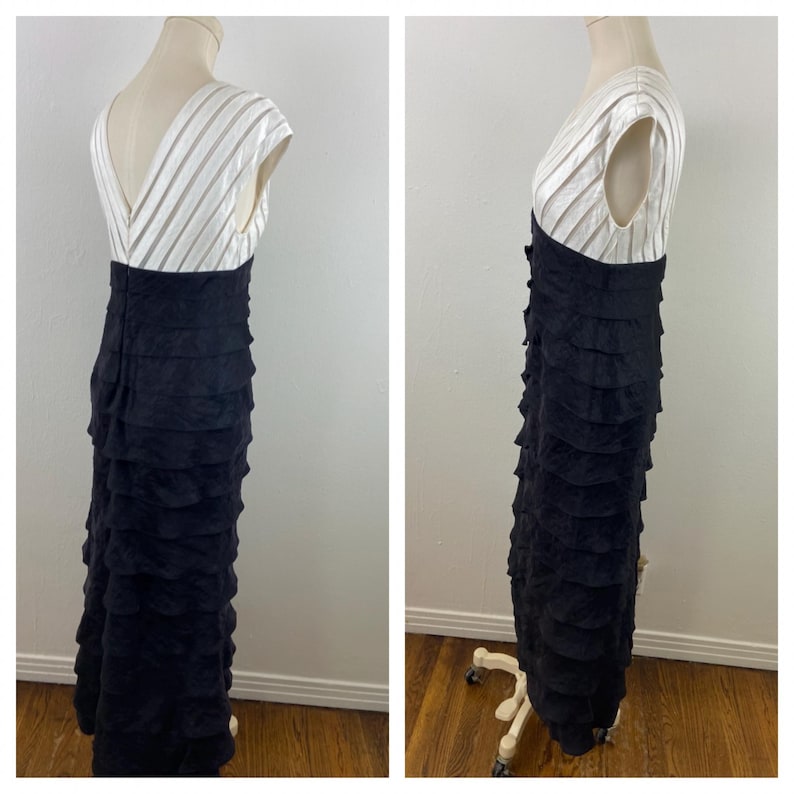 May include: A formal, floor-length dress with a white, striped bodice and a black, tiered skirt. The dress has a V-neck and cap sleeves. The skirt is made of multiple layers of fabric, creating a ruffled effect. The dress is displayed on a mannequin.