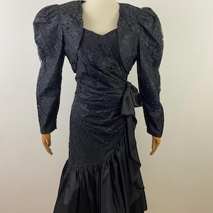 May include: A black lace dress with a matching lace jacket. The dress has a sweetheart neckline and a ruffled skirt. The jacket has puffed sleeves.