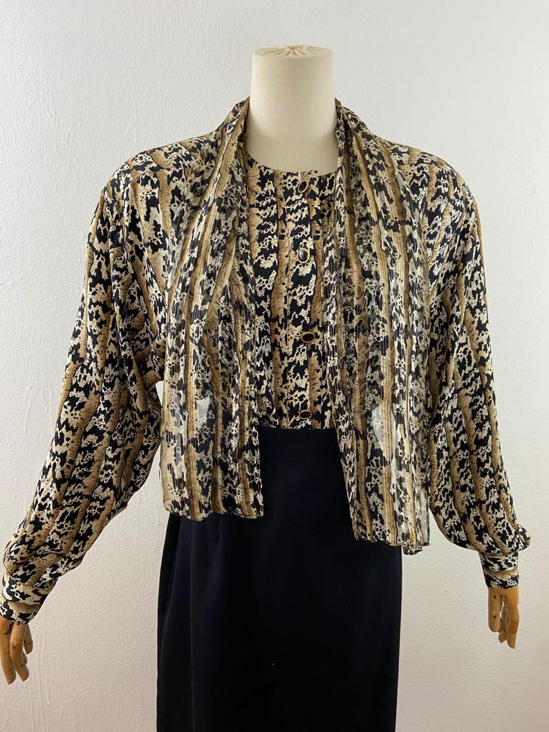 Peut inclure: Ensemble deux pi&egrave;ces vintage. Le haut pr&eacute;sente un imprim&eacute; animalier marron, noir et blanc avec des manches longues et un col drap&eacute;. La jupe est noire. L'ensemble est pr&eacute;sent&eacute; sur un mannequin.