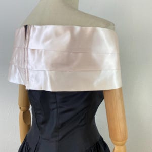 Pu&ograve; includere: Un abito nero a spalle scoperte con un'applicazione in raso rosa. L'abito ha un corpetto aderente e una gonna ampia.