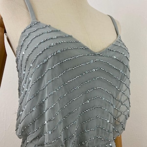 K&ouml;nnte beinhalten: Hellblaues Kleid mit V-Ausschnitt und Spaghettitr&auml;gern. Das Kleid ist mit Reihen aus silbernen Pailletten verziert, die einen schimmernden Effekt erzeugen. Das Kleid wird auf einer Schaufensterpuppe pr&auml;sentiert.