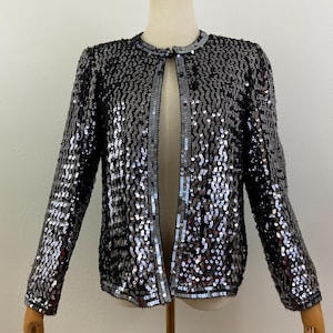 May include: A silver and black sequined jacket with a button closure. The jacket has long sleeves and a fitted silhouette.
