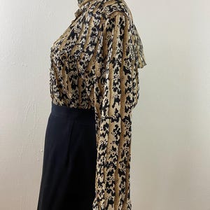 Peut inclure: Ensemble vintage compos&eacute; d'un chemisier et d'une jupe. Le chemisier pr&eacute;sente un col montant et des manches longues avec un imprim&eacute; animalier beige, noir et cr&egrave;me. La jupe est noire unie, de longueur genou. L'ensemble est pr&eacute;sent&eacute; sur un mannequin.