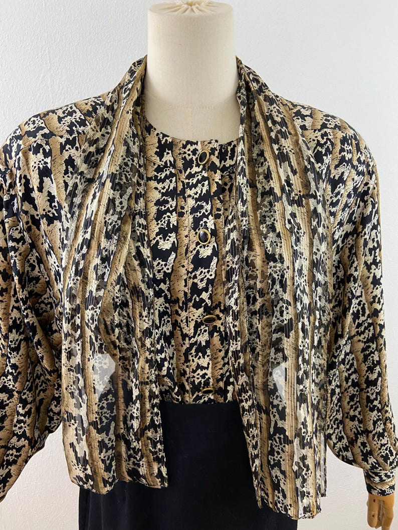 Peut inclure: Ensemble vintage compos&eacute; d'un chemisier et d'une veste &agrave; imprim&eacute; animal. Le chemisier pr&eacute;sente un devant boutonn&eacute; et un col. La veste assortie a des manches longues. L'imprim&eacute; est un m&eacute;lange de noir, de marron et de beige.
