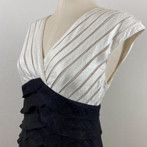 May include: A formal dress with a V-neck bodice and a layered skirt. The bodice is white with horizontal stripes, and the skirt is black with a tiered, ruffled design. The dress is displayed on a mannequin.