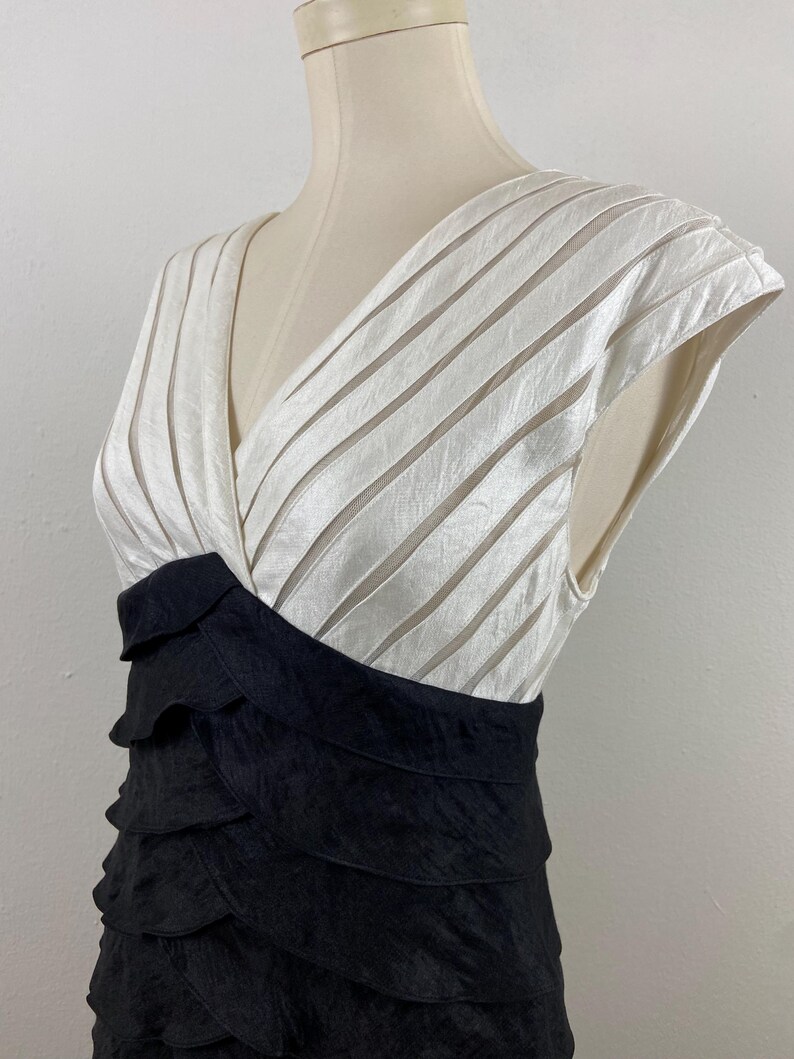 May include: A formal dress with a V-neck bodice and a layered skirt. The bodice is white with horizontal stripes, and the skirt is black with a tiered, ruffled design. The dress is displayed on a mannequin.