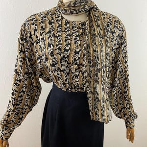 Peut inclure: Ensemble vintage compos&eacute; d'un chemisier et d'une jupe. Le chemisier pr&eacute;sente un imprim&eacute; animalier marron, noir et beige avec des manches longues et une &eacute;charpe assortie. La jupe est noire unie, taille haute. Le chemisier a des boutons dor&eacute;s.