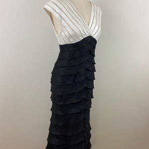 May include: A formal, floor-length dress with a layered black skirt and a white bodice. The bodice features a V-neck and horizontal striped detailing. The dress is displayed on a mannequin.