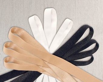 May include: A close-up of three different types of elastic ribbon. The ribbon is in black, white, and beige. The ribbon is arranged in a fan shape.