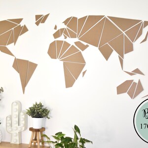 Peut inclure: Une grande carte du monde géométrique en carton brun, montée sur un mur blanc. La carte mesure 170 x 80 cm. La carte est entourée de plantes et d'un cactus blanc.