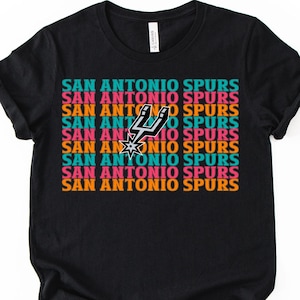 May include: Black t-shirt featuring the text "SAN ANTONIO SPURS" in a repeating pattern of teal, orange, pink, and white. The Spurs logo is centered on the shirt.