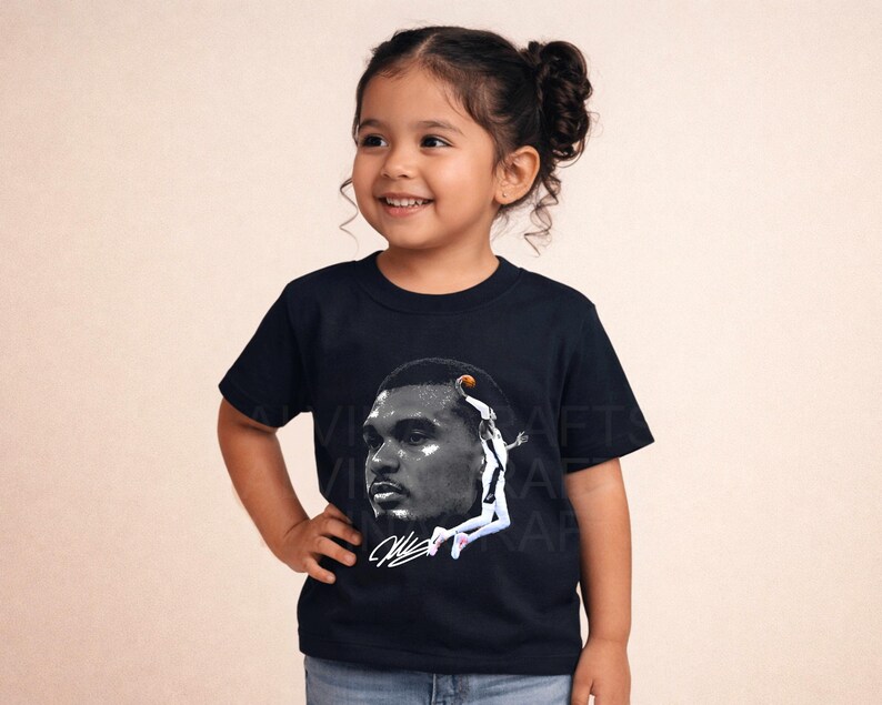 May include: A navy blue t-shirt featuring a black and white image of a basketball player. The image includes a signature and a basketball. The t-shirt is being worn by a young child.