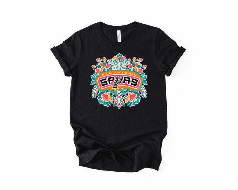 May include: A white ceramic mug with a black handle and the text "But First, Coffee" in a black, handwritten-style font. The mug is on a white surface.