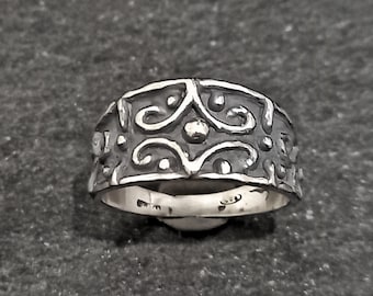 Puede incluir: Un anillo de plata con un diseño ornamentado y texturizado. El anillo presenta un patrón repetitivo de espirales y puntos, creando una apariencia detallada y llamativa. La banda es ancha y el estilo general es vintage o antiguo.