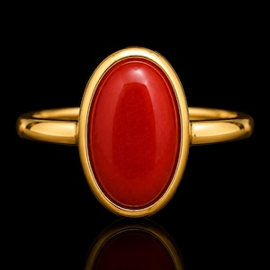 May include: A gold ring featuring a smooth, oval-shaped red stone set in a polished gold bezel. The band is simple and rounded, showcasing a high-shine metallic finish that complements the vibrant, solid red color of the central gemstone setting.