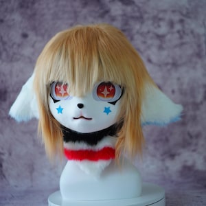 May include: A white and tan furry mask with large, expressive eyes featuring starburst designs. The mask has light brown hair, blue star accents, and a black, red, and white collar. The ears are white with blue tips.