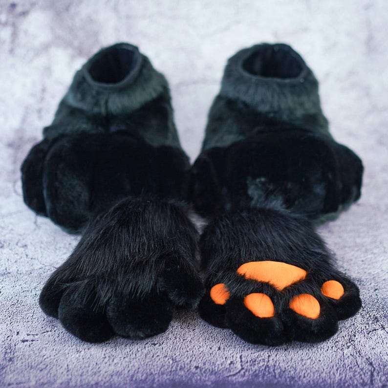 Pu&ograve; includere: Un paio di pantofole di pelliccia nera a forma di zampa con cuscinetti per zampe arancioni. Le pantofole sono realizzate in tessuto morbido e peluche e hanno una vestibilit&agrave; comoda.
