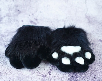 May include: A pair of black furry paw-shaped hand warmers with white paw pads. The hand warmers are soft and plush.