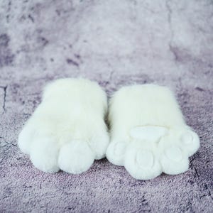 May include: A pair of white furry paw-shaped hand warmers with a white felt paw pad on each.