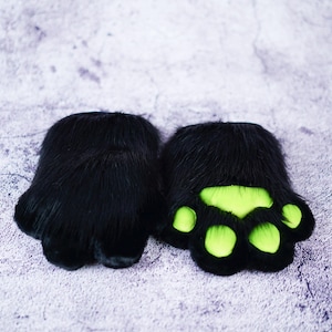 May include: A pair of black furry paw-shaped hand warmers with green paw pads.
