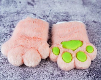 May include: A pair of pink furry paw gloves with green paw pads. The gloves are made of soft, plush fabric and have a realistic paw design.
