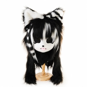 Può includere: Un cappello di peluche a tema animale con lunga pelliccia sintetica nera e bianca, orecchie a punta con dettagli interni bianchi e una maschera facciale bianca con grandi fori neri per gli occhi, un piccolo naso nero e una piccola lingua rosa.