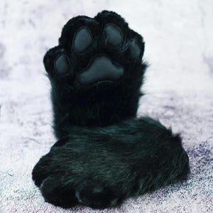 Puede incluir: Un par de guantes de pata de piel sint&eacute;tica negra, con una almohadilla de pata detallada y almohadillas individuales para los dedos de los pies. Los guantes est&aacute;n dise&ntilde;ados para parecerse a las patas de un gato u otro animal, con una textura suave y afelpada.