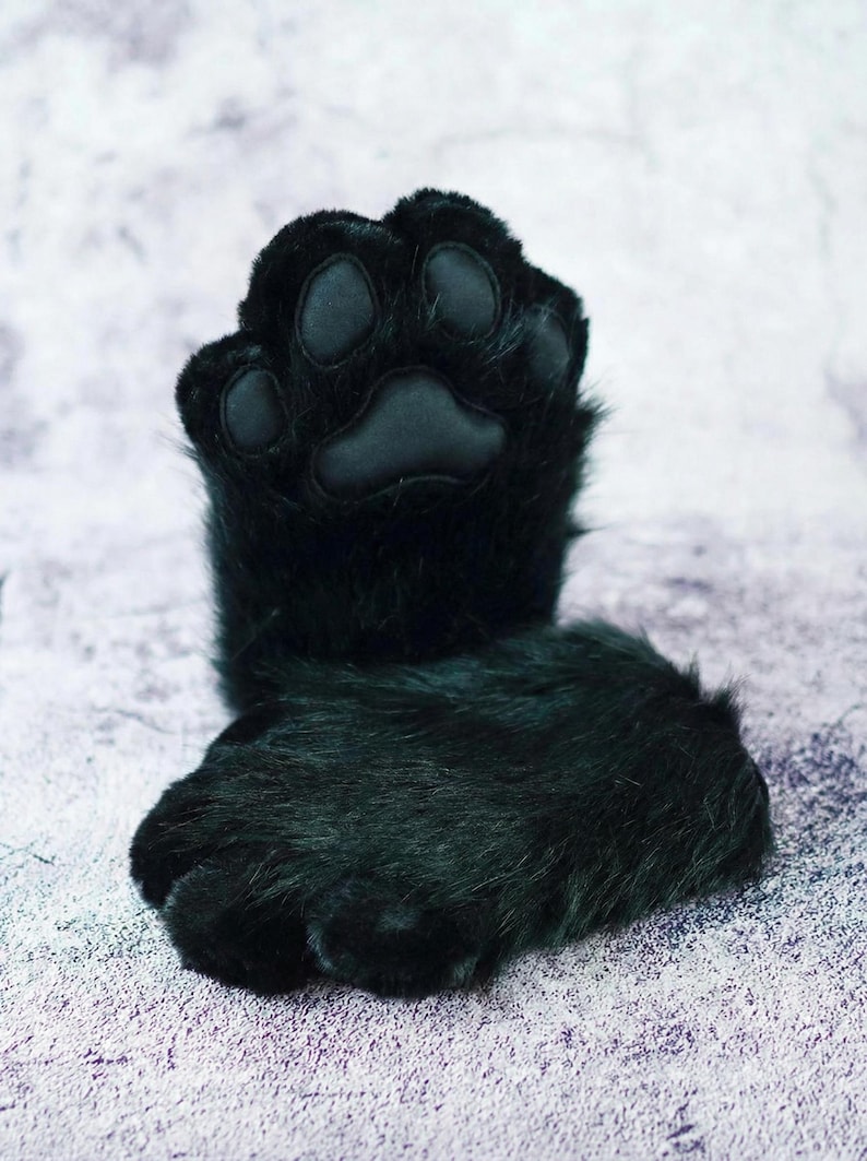 Puede incluir: Un par de guantes de pata de piel sint&eacute;tica negra, con una almohadilla de pata detallada y almohadillas individuales para los dedos de los pies. Los guantes est&aacute;n dise&ntilde;ados para parecerse a las patas de un gato u otro animal, con una textura suave y afelpada.