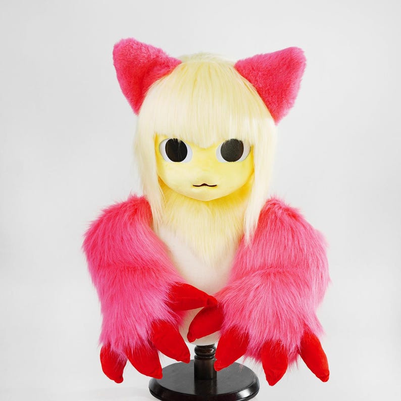 May include: A creature headpiece featuring pale yellow faux fur, straight blonde hair with bangs, and two bright pink pointed ears. The piece includes long, shaggy pink fur sections on the sides with prominent, solid red claw-like appendages.