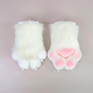 May include: A pair of white faux fur animal paw gloves featuring long, soft white synthetic fur, light pink padded paw pads on the underside, and pointed white claws extending from the tips of each of the four fingers on both gloves.
