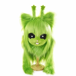 May include: A bright lime green faux fur mask featuring large black oval eyes with white pupils, a small pink nose, and a protruding tongue. Two tall antennae topped with green stars extend from the top of the head, which is covered in long, shaggy green fur.