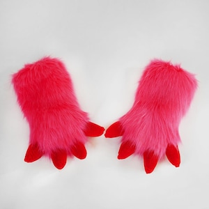 May include: A pair of bright pink faux fur gloves featuring long, shaggy synthetic fibers and four distinct, solid red fabric claws extending from the fingertips of each glove, designed with a wide opening for the hand to slide into easily.
