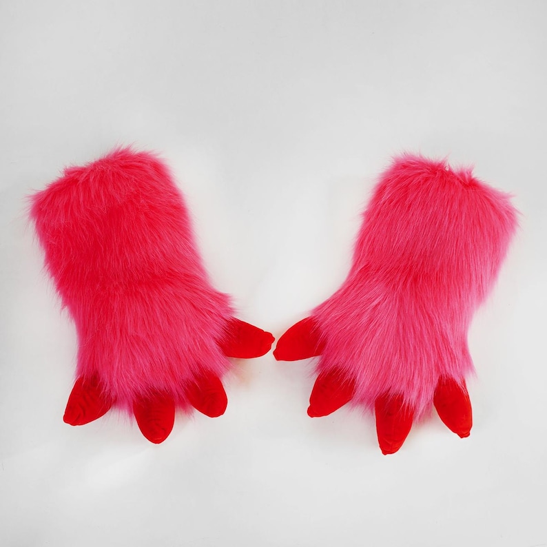 May include: A pair of bright pink faux fur gloves featuring long, shaggy synthetic fibers and four distinct, solid red fabric claws extending from the fingertips of each glove, designed with a wide opening for the hand to slide into easily.