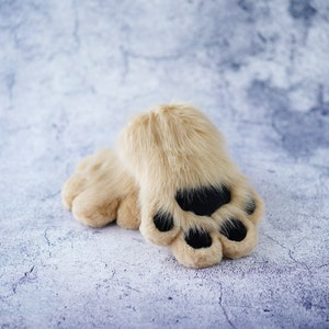 May include: A pair of fluffy brown slippers with black paw prints on the toes. The slippers are made of soft, plush fabric and are perfect for keeping your feet warm and cozy.
