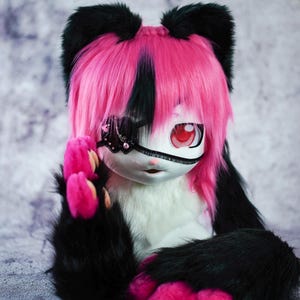 May include: A plush toy with black and white fur, pink paws, and a pink and black wig. The toy has a black eye patch with a sparkly design and one red eye.