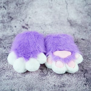 May include: A pair of purple fuzzy cat paw hand warmers with white paw pads and pink paw pads.