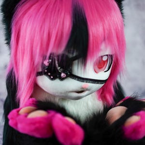 May include: A plush toy with pink and black fur, wearing a black eye patch with a butterfly design. The toy has red eyes and a white face.