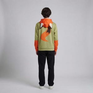 Pu&ograve; includere: Una felpa con cappuccio verde con dettagli arancioni e un design a volpe. Il cappuccio &egrave; arancione con dettagli di orecchie di volpe bianche e marroni. La parte posteriore della felpa presenta un grande design a coda di volpe arancione. Le maniche hanno polsini arancioni.