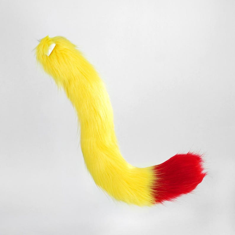 May include: A long, curved faux fur tail accessory featuring a vibrant yellow main section that transitions into a bright red tip. The plush, textured material is designed with a slight curve, showcasing a soft, shaggy appearance throughout the length of the piece.